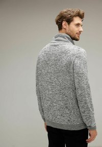 Suéter gris de punto con cuello alto, que presenta un patrón texturizado y un dobladillo y puños acanalados. La tela parece suave y versátil.