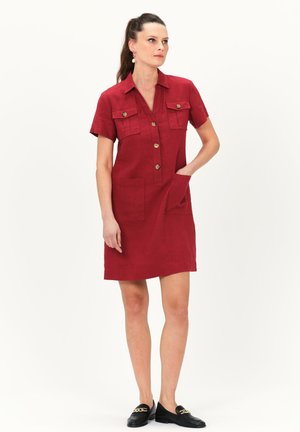 Red linen shirt dress with a button front, short sleeves, two chest pockets, and side pockets, featuring a smooth texture and tailored fit.