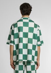 Camicetta a maniche corte con motivo a scacchi verde e bianco. Realizzata in tessuto morbido con una vestibilità rilassata e un design con colletto.
