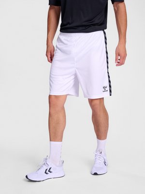 Mand iført hvide sportsshorts med sorte sidelister og logo, kombineret med hvide sokker og hvide atletiksko, stående mod en ensfarvet baggrund.