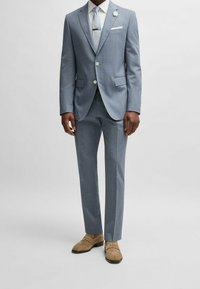 Ljusblå kostym med texturerad yta, med en tvåknappars kavaj, matchande byxor och en vit näsduk. Bruna loafers fulländar outfiten.