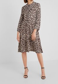 Leopardenmuster-Kleid aus leichtem Material, mit langen Ärmeln, einem runden Ausschnitt und einem gestuften Saum. Kombiniert mit schwarzen Sandalen mit Riemen.