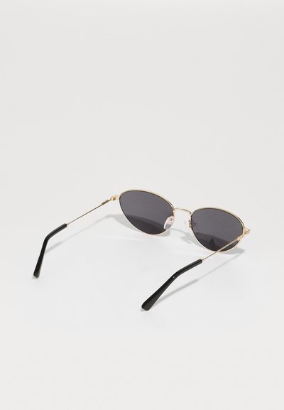 Gold-framed sunglasses with oval dark lenses, featuring black tips on the temples and clear silicone nose pads for comfort.