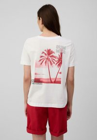 T-shirt en coton blanc avec un graphique rouge de palmiers et le texte "ÉTÉ" ainsi que "DÉTENDU RAFRAÎCHI RECHARGÉ" au dos.