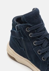 Scarpa high-top in suede blu con dettagli in rete, lacci tondi e occhielli metallici. Presenta una cerniera laterale e una suola in gomma beige.