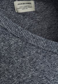 Grau melierter Strickpullover mit Rundhalsausschnitt, gerippten Bündchen und Saum. Innen sichtbares Etikett mit Markennamen. Weicher Stoff.