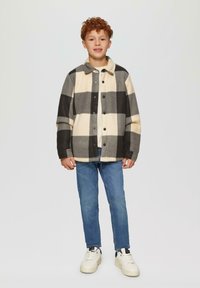 Kurtka z włóczki w kratę w odcieniach kremowym, czarnym i szarym; z guzikami z przodu i kołnierzem; noszona z niebieskimi dżinsami oraz białymi trampkami.