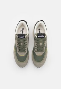 Sneakers verdi e grigie con superiore in rete, dettagli in camoscio, oblò posteriori neri e cuciture gialle. Presentano lacci rotondi e linguetta imbottita.