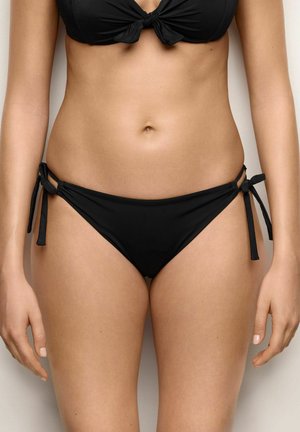 Damski tors w czarnym bikini z wiązanymi po bokach majtkami i wiązanym stanikiem, przedstawiony na jednolitym białym tle.