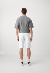 Sudadera gris de manga corta, pantalones cortos blancos y zapatillas ligeras con detalles oscuros. Vista trasera que muestra un ajuste holgado y un estilo casual.