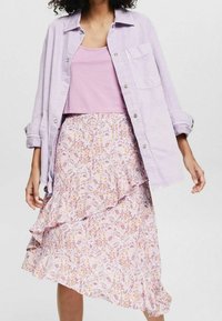 Camicia lavanda a bottoni sopra una canotta rosa, abbinata a una gonna floreale a strati con motivi rosa, gialli e bianchi.