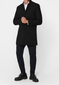 Zwarte wollen mix jas met een getailleerde pasvorm, lange mouwen en een enkelvoudig knoopdesign. Draag het over een gestreept wit shirt en marineblauwe broek.