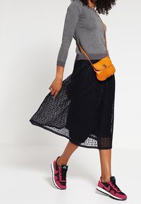 Grå langærmet bluse, sort plisseret midiskørt, orange crossbody taske og pink Nike sneakers. Har tekstureret stof og casual stil.
