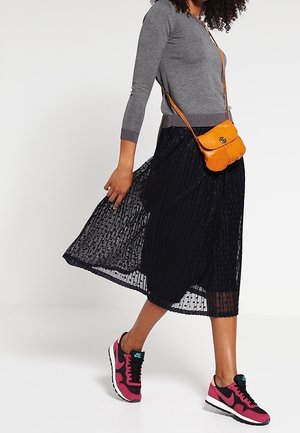 Grå långärmad topp, svart plisserad midi kjol, orange crossbody-väska, och rosa Nike-sneakers. Har texturerad tyg och avslappnad stil.