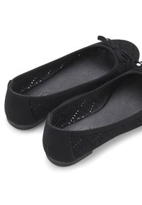 Schwarze Ballettschuhe aus weichem Material mit Ausschnittmustern. Verfügt über ein glattes Innenfutter und ein kleines Schleifenakzent auf der Vorderseite.