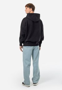Schwarzer Hoodie mit geräumiger Kapuze und gerippten Bündchen, kombiniert mit hellblauen Jeans im Straight-Leg-Stil und schwarzen Sneakers.