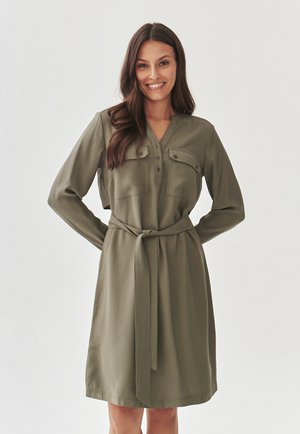 Olive green dress with long sleeves, button-down front, two chest pockets, and a tied waist belt. Smooth fabric with a classic silhouette.