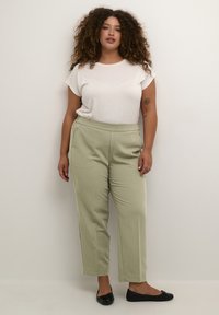 Pantalons ajustés vert clair avec une texture lisse et une taille élastique, associés à un t-shirt blanc à manches courtes et des ballerines noires.