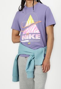 Nike purple t-shirt featuring a graphic of a striped pyramid, paired with gray sweatpants and a light blue sweater tied around the waist.
