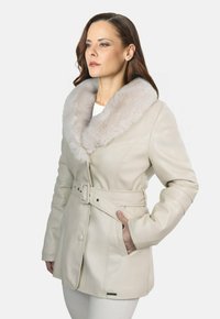 Chaqueta de cuero beige con un amplio cuello de piel gris claro, con cinturón en la cintura y bolsillos laterales; textura suave con costuras detalladas.