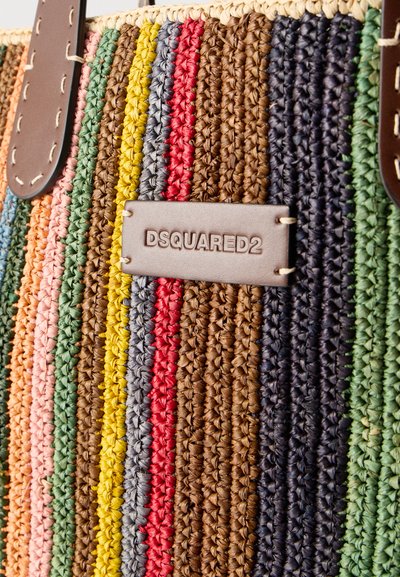Gros plan sur un sac tissé multicolore à rayures horizontales, avec une étiquette en cuir embossée de "DSQUARED2" et des anses en cuir.