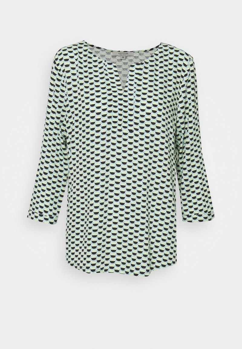 Blouse à manches longues avec encolure arrondie et entaille, présentant un motif répétitif de demi-cercles noirs et vert clair sur tissu blanc.