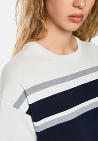 Knitted sweatshirt featuring horizontal stripes in navy, white, and gray. Ribbed crew neckline and soft texture. Close-up of the fabric.