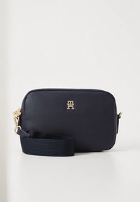 Navy leren crossbodytas met een gladde textuur, gouden hardware en een afneembare, geweven riem; voorzien van een logo-accent aan de voorkant.