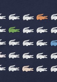 Μπλε ναυτικό μπλουζάκι με επαναλαμβανόμενο μοτίβο γραφικών κροκοδ είλων σε λευκό, πορτοκαλί, πράσινο, ανοιχτό ροζ και μπλε. Μαλακό βαμβακερό ύφασμα.