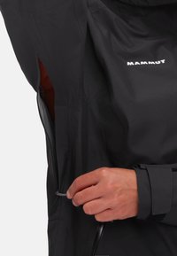 Schwarze wasserdichte Jacke aus strukturiertem Stoff, mit einer Reißverschlusstasche und verstellbaren Manschetten. Logo auf der Vorderseite sichtbar.