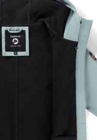 Lichtblauwe jasseninterieur met zwarte fleece voering, voorzien van een stoffen label dat is bevestigd in het nekgebied en drukknoopsluitingen langs de rand.