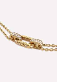 Goldene Halskette mit Gliedern, die mit klaren Strasssteinen verziert sind und eingravierten "GUESS"-Akzenten. Glatte Metalloberfläche, polierte Textur.
