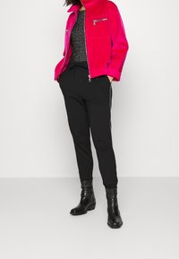 Fuksjowa kurtka na zamek błyskawiczny z kieszenią na piersi, zestawiona z czarnymi joggerami z bocznymi paskami oraz czarnymi botkami za kostkę. Pod spodem teksturowany sweter.