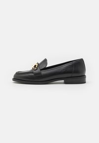 Mocassins en cuir noir avec un petit talon, ornés d'un accent en métal doré sur la bride, texture lisse et design classique.