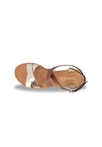 Brown leather sandal with gold and white cross straps, flat sole, and ankle buckle. Notable stitching and brand logo on the insole.