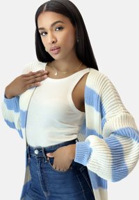 Gestreifter Cardigan aus weichem Strick in Blau- und Weißtönen; getragen über einem weißen gerippten Tanktop und hochsitztenden Jeans.