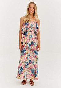 Kwiatowa sukienka maxi z falbaną na górze, z różowymi, niebieskimi i żółtymi kwiatami na jasnym tle. Noszona z brązowymi sandałami.
