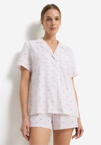 Σετ πιτζάμες με κοντά μανίκια σε ανοιχτό ροζ ύφασμα με λεπτές λευκές ρίγες, διακοσμημένο με μικρά κόκκινα σχέδια καρδιάς και μπροστινό μέρος με κουμπιά.