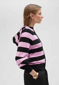 Felpa con zip a righe nere e rosa, dotata di cappuccio, polsini a costine e un pannello testurizzato sul petto. Tessuto morbido con vestibilità comoda.