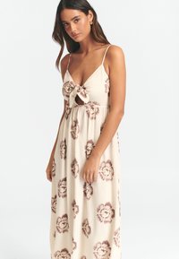 Maxi šaty v béžové barvě s hlubokým V výstřihem a nastavitelnými ramínky. Mají přední uzel a hnědý květinový vzor po celé ploše. Měkká, splývavá látka.