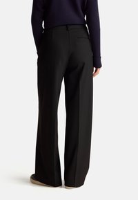 Black wide-leg trousers made of smooth fabric, featuring a flat front and back pocket. Paired with a navy ribbed sweater for contrast.