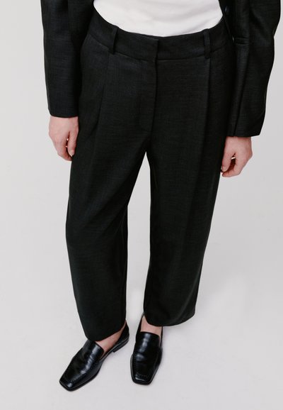 Pantaloni neri su misura con tessuto strutturato, pieghe frontali e una vita standard. Abbinati a mocassini neri per un aspetto coeso.