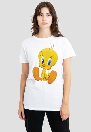 Woman with wavy brown hair wears a white T-shirt featuring a large, colorful Tweety Bird cartoon sitting with orange feet forward.