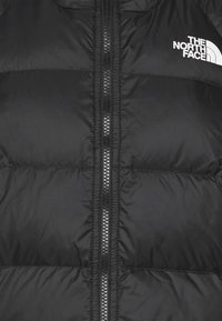 Zwarte pufferjas met ritssluiting, voorzien van een doorgestikt ontwerp en het witte logo van The North Face aan de linkerbovenkant.