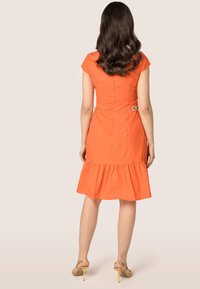 Oranje aansluitend jurk met een flared zoom, korte mouwen en een taille die is geaccentueerd met een gouden kettingriem. Glad textuur van de stof, tot de knie.