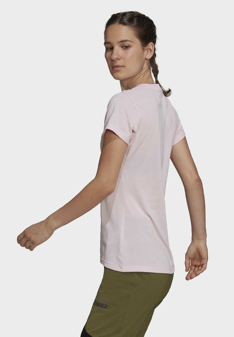 Helles rosa, kurzärmliges Sport-T-Shirt aus strukturiertem Stoff mit Rippdesign, kombiniert mit grünen Outdoor-Hosen, die ein Logo tragen.
