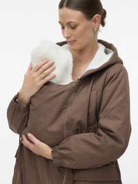 Woman wearing brown zipped jacket with white fleece lining, holding a baby wrapped inside the jacket close to her chest.