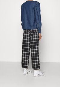 Blusa di denim a maniche lunghe con collo rotondo e maniche a sbuffo, abbinata a pantaloni larghi a quadri bianchi e neri e sneakers bianche.