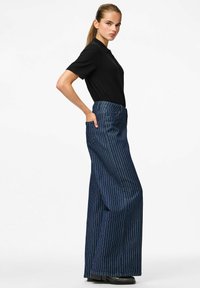 Augstās jostas daļas plašas bikses tumši zilā džinsā ar baltām vertikālām svītrām. Iespējas sānu kabatām un tīrai, izsmalcinātai siluetam.