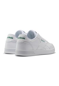 Valkoiset nahkakengät, joissa on teksturoitu pinta, pyöristetty varvas ja vihreä Reebok-logo kantapään kohdalla; varustettu pehmustetulla kauluksella ja kumipohjalla.